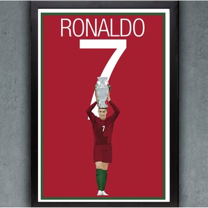 K&ouml;nnte beinhalten: Gerahmter Druck mit Cristiano Ronaldo, der eine Troph&auml;e h&auml;lt. Der Hintergrund ist rot mit dem Namen "RONALDO" und der Zahl "7" in Wei&szlig;. Der Spieler tr&auml;gt eine weinrote Uniform mit gr&uuml;nen Socken.