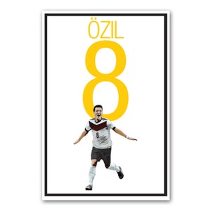 May include: A framed poster featuring a soccer player in a white, black, and red uniform with the number 8. The name "ÖZIL" is above a large yellow number 8. The player is celebrating with arms outstretched.