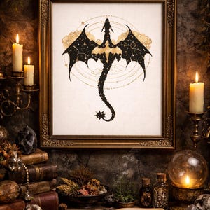 Könnte beinhalten: Ein gerahmtes Kreuzstichbild eines Drachen mit schwarzen Flügeln und Körper und einem goldenen Bauch. Der Drache ist vor einem weißen Hintergrund mit goldenen Akzenten platziert. Der Rahmen ist verziert und golden. Das Bild ist von Kerzen, Büchern und anderen mystischen Gegenständen umgeben.