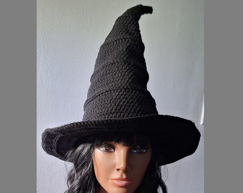 May include: A black crocheted witch hat with a tall, pointed crown and a wide brim. The hat is worn by a person with dark hair.