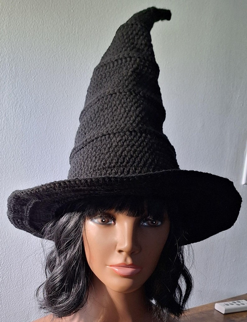 May include: A black crocheted witch hat with a tall, pointed crown and a wide brim. The hat is made with a textured stitch and has a slightly curved brim.