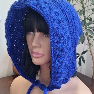 May include: A vibrant blue crocheted hood with a textured pattern. The hood features a drawstring closure and is displayed on a mannequin. The crochet work is detailed, showcasing the craftsmanship of the handmade item.