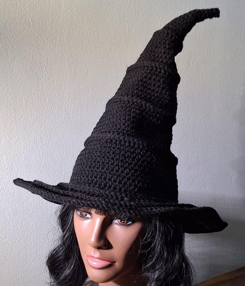 May include: A black crocheted witch hat with a tall, pointed crown and a wide brim. The hat is worn by a person with long black hair.