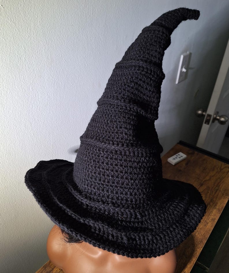 May include: A black crocheted witch hat with a tall, pointed crown and a wide brim. The hat is made with a textured stitch and has a spiral design.