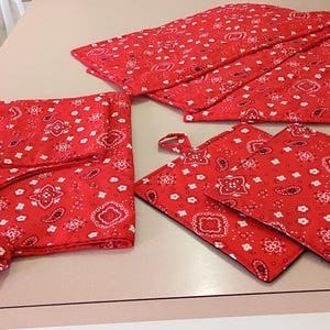 May include: A red kitchen set with a white paisley pattern. The set includes an apron with ties, four pot holders, and four matching placemats. The items are made of a quilted fabric.