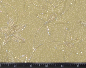 May include: Close-up of a pale yellow fabric with an embroidered floral pattern. The design features stylized flowers and vines, embellished with small, shiny beads. The background has a subtle, swirling texture. The fabric is likely used for apparel or home decor.