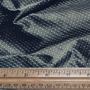 May include: Close-up of a dark gray fabric with a subtle, repeating white dot pattern. A wooden ruler with inch markings is at the bottom, providing scale. The fabric is slightly wrinkled, showing texture and depth.