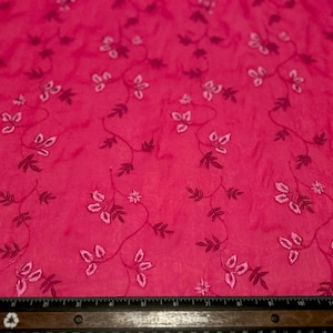 May include: A vibrant hot pink fabric featuring a delicate embroidered pattern of winding vines with small leaves and flowers in darker pink tones. A black ruler is positioned at the bottom, showing a measurement scale of up to 12 inches.