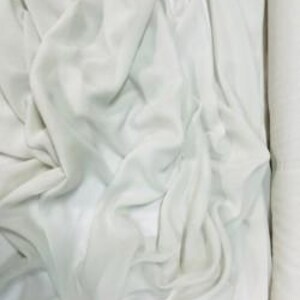 May include: Close-up of a roll of light green fabric. The fabric is draped and folded, showing the texture and flow of the material. The fabric is a solid colour and appears to be soft and lightweight.