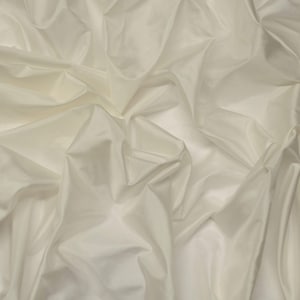 Op de afbeelding: Crèmekleurige stof met een zijdeachtige glans, vakkundig gedrapeerd en gevouwen. De textuur van de stof is zichtbaar, met zachte schaduwen en highlights die diepte creëren. Het materiaal oogt glad en luxueus, geschikt voor kleding of interieurdecoratie.