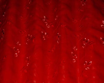 May include: A deep red fabric featuring a subtle, tonal embroidered pattern of delicate leaves and small floral sprigs. The material has a soft, slightly gathered texture that creates gentle folds and shadows across the surface of the textile.