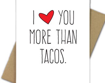 May include: A white greeting card with the text "I ❤️ YOU MORE THAN TACOS" in black, with a red heart. The card is inside a brown envelope, ideal for expressing affection.