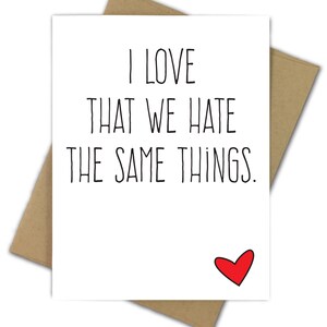May include: A white greeting card with the text "I LOVE THAT WE HATE THE SAME THINGS" in black, with a small red heart at the bottom right. The card is inside a brown envelope.
