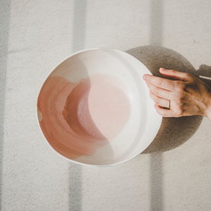 May include: A white ceramic bowl with a pink glaze inside. The bowl is sitting on a light gray surface.