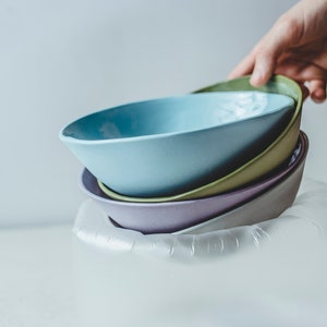Pode incluir: Um conjunto de quatro tigelas de cerâmica em vários tons de azul, verde e roxo, aninhadas dentro de um recipiente protetor de plástico transparente.