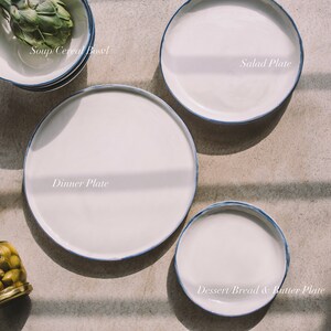 May include: A set of four white ceramic plates with blue trim. The plates are arranged in a circle, with the largest plate in the center and the smallest plate on the top. The plates are labeled "Dinner Plate", "Salad Plate", "Soup/Cereal Bowl", and "Dessert/Bread & Butter Plate".