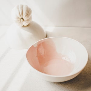 May include: A white ceramic bowl with a pink interior. The bowl is empty and sitting on a white surface.