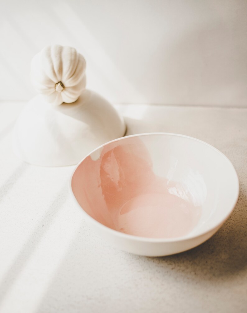 May include: A white ceramic bowl with a pink interior. The bowl is empty and sitting on a white surface.