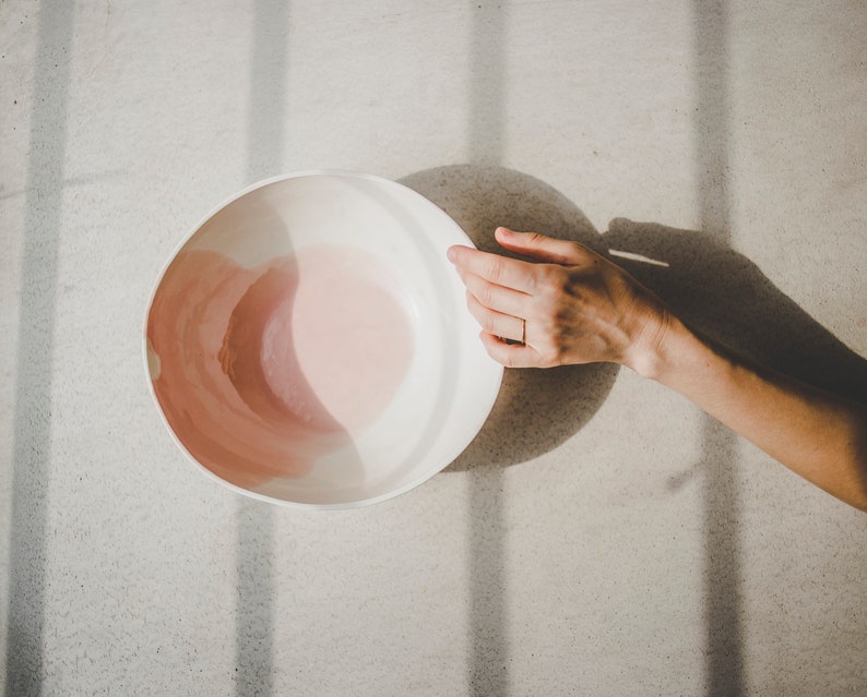 May include: A white ceramic bowl with a pink glaze inside. The bowl is sitting on a light gray surface.