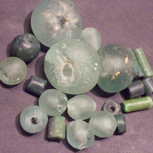 Puede incluir: Una colección de cuentas de vidrio verde, algunas con agujeros en el centro y otras con una superficie lisa. Las cuentas son de varios tamaños y formas.