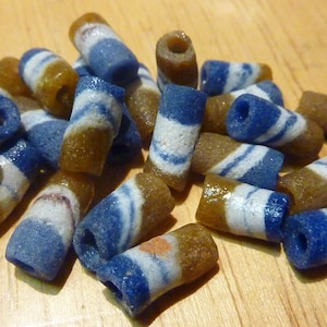 以下が含まれることがあります： 白のストライプが入った茶色と青のガラスビーズのセット。ビーズは円筒形で、滑らかで磨かれた仕上げになっています。