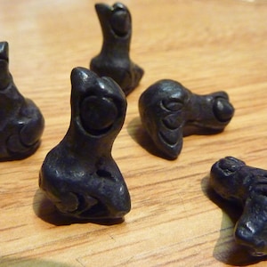 May include: Five small black ceramic figurines of birds with detailed carvings. The birds are in various poses, some with their heads tilted up and others with their heads down.