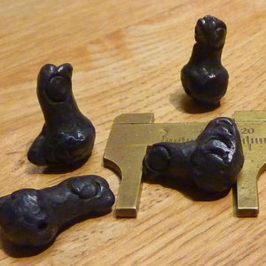 May include: Five small black ceramic figurines shaped like birds. The figurines are arranged on a wooden surface with a ruler for scale.