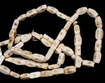 May include: A strand of off-white bone beads with a carved swirl design. The beads are strung together to form a necklace or bracelet.