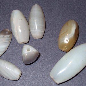 May include: Seven agate beads in various shades of white and brown, with some showing a swirl pattern. The beads are oval and round in shape.