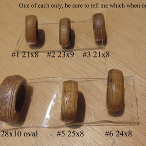 May include: Six wooden rings with different sizes and patterns. The rings are labeled with numbers and measurements in inches. The rings are arranged in two rows on a wooden surface.