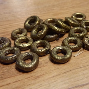 May include: A group of 17 gold-colored metal rings, each with a slightly different size and shape. The rings are arranged in a pile on a wooden surface.