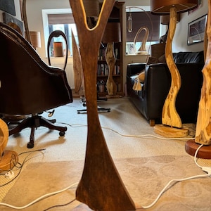 May include: A wooden lamp with a unique Y-shaped design. The lamp is made of dark brown wood and has a natural wood base. The lamp is lit and casting a warm glow on the surrounding furniture.