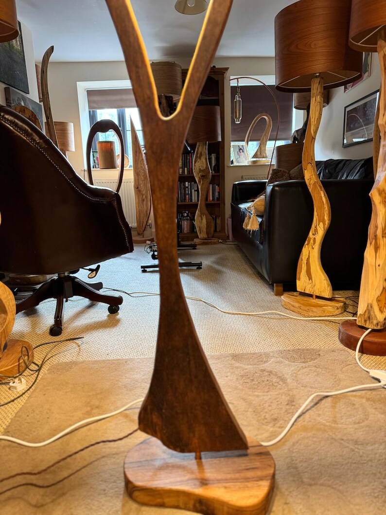 May include: A wooden lamp with a unique Y-shaped design. The lamp is made of dark brown wood and has a natural wood base. The lamp is lit and casting a warm glow on the surrounding furniture.