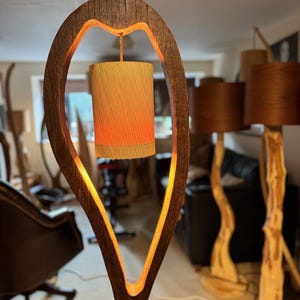 May include: A wooden lamp with a unique, heart-shaped design. The lamp features a warm, glowing light emanating from a cylindrical shade.