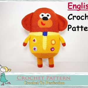 May include: Crochet pattern for a brown and yellow dog with a blue and white collar. The pattern is titled "English Crochet Pattern" and "Crochet To Perfection".