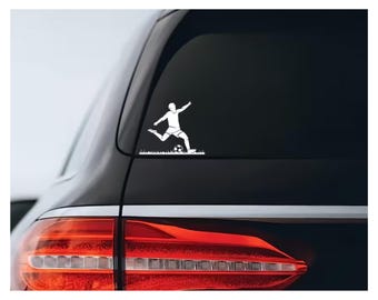 May include: White vinyl decal of a soccer player kicking a ball. The decal is applied to the rear window of a black car. The player is in mid-kick, with the ball on the ground and a line of grass below.