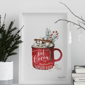 May include: White framed print with a watercolor illustration of a red mug filled with hot cocoa, marshmallows, whipped cream, cinnamon sticks, and a candy cane. The text reads "Hot Cocoa with marshmallows SERVED HERE".