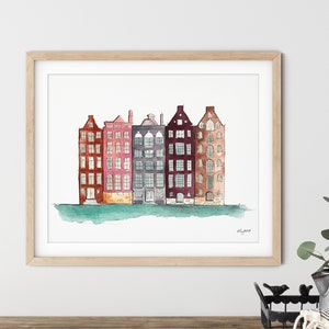 May include: Watercolor painting of a row of five colorful buildings with windows and doors. The buildings are painted in shades of red, pink, purple, gray, and brown. The buildings are set against a light blue background with a green water line at the bottom.