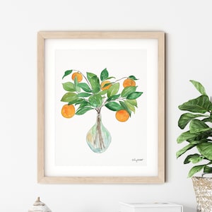 May include: Watercolor painting of a vase with orange fruit and green leaves. The vase is clear glass and the fruit is a bright orange color. The leaves are a deep green color. The painting is framed in a light wood frame.