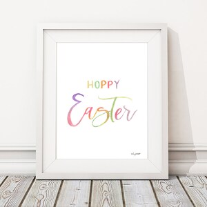 May include: A white framed print with the text "Hoppy Easter" in colorful watercolor lettering.