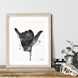 May include: Black and white watercolor painting of a hand making the shaka sign, a popular Hawaiian gesture of peace, aloha, and good vibes. The hand is dripping with black paint, creating a dynamic and artistic effect.