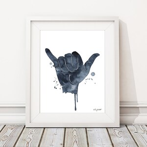 May include: A watercolor painting of a hand making the shaka sign, a popular Hawaiian gesture of peace, aloha, and good vibes. The hand is painted in shades of blue and gray, with drips of paint extending from the fingers. The background is white.