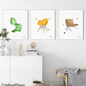 May include: Three watercolor illustrations of chairs, each framed in white. The first chair is green and has a curved back. The second chair is yellow and has a four-legged base. The third chair is brown and has a metal frame.
