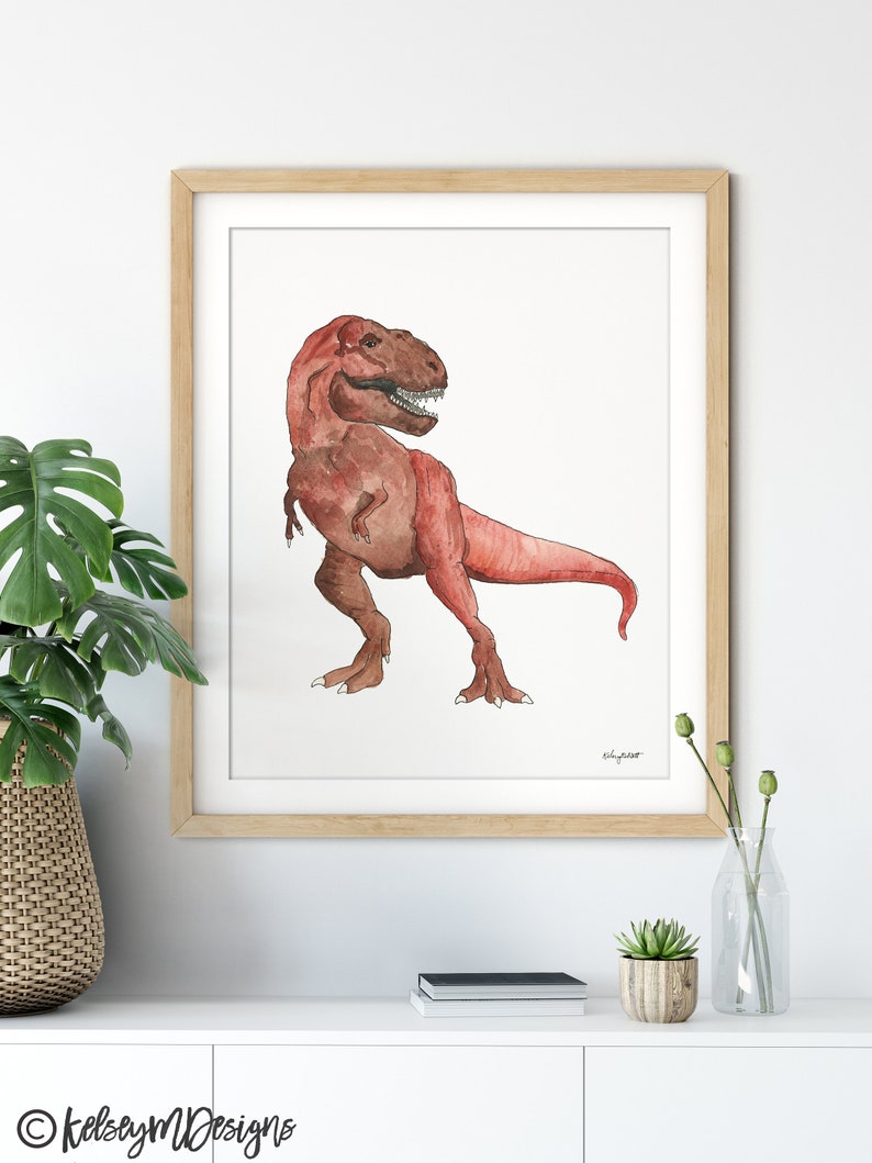 May include: Watercolor painting of a Tyrannosaurus Rex in shades of red and brown, framed in a light wood frame. The dinosaur is depicted in a side profile, with its mouth open. The artwork is signed by the artist.