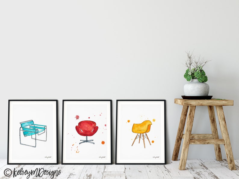 May include: Three framed watercolor illustrations of iconic chairs. The first chair is a blue and white lounge chair. The second chair is a red egg chair. The third chair is a yellow and brown Eames chair.