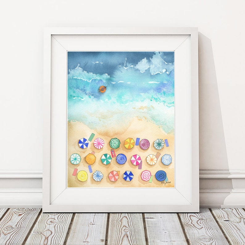 May include: A watercolour painting of a beach scene with colourful umbrellas and a small boat in the ocean. The painting is framed in a white frame.