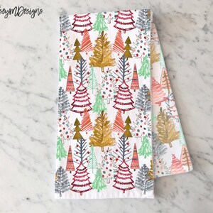 May include: White kitchen towel with a repeating pattern of colorful Christmas trees in shades of red, green, gold, and blue. The trees are stylized with various designs. The text "kelseymDesigns" is in the upper left corner.