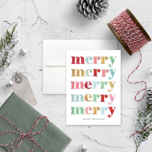 May include: A white card with the word "merry" repeated five times in different colors. Each "merry" is in a different color: red, gold, pink, teal, and gold. The text "Happy Holidays" is printed below the five "merry" words.