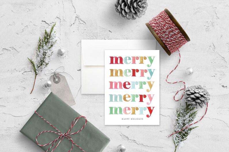 May include: A white card with the word "merry" repeated five times in different colors. Each "merry" is in a different color: red, gold, pink, teal, and gold. The text "Happy Holidays" is printed below the five "merry" words.