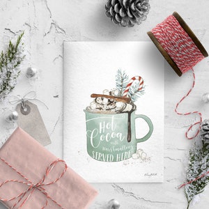 Puede incluir: Una tarjeta blanca con una ilustraci&oacute;n de acuarela de una taza verde llena de chocolate caliente, malvaviscos, crema batida, un palo de canela y un bast&oacute;n de caramelo. El texto en la tarjeta dice "Hot Cocoa with marshmallows SERVED HERE".